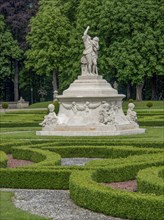 Monumental fountain with several sculptures in a well-kept baroque garden, park with green hedges,