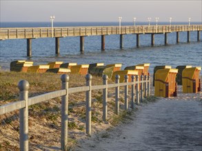 Several beach chairs on a sandy path leading to a jetty into the sea at sunset, beach chairs in the
