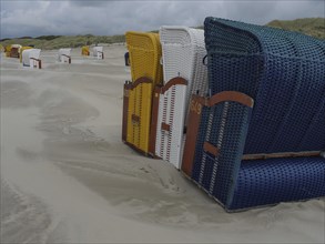 Colourful beach chairs standing in a row on a sandy beach under a cloudy sky, colourful beach