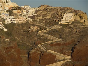 A rocky landscape on Santorini with houses on cliffs and winding stairs, illuminated by golden