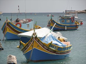 Several colourfully painted fishing boats anchor quietly in a harbour, surrounded by ropes and