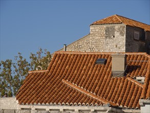 Close-up of a stone building with red-tiled rooftops and a chimney, under a blue sky with detailed