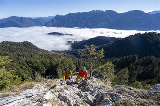 Two friends, mountaineers climbing the via ferrata to the rocky summit of the Ettaler Manndl, view