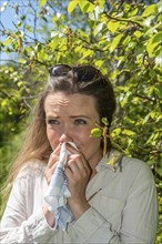 Young Caucasian woman, 35 years old, with allergy stands by flowering birch (Betula) in Ystad,