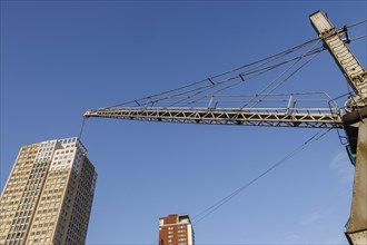 A crane towers over modern skyscrapers under a blue sky in a city scene, small harbour in a big