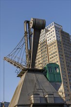 Steel crane in front of a modern skyscraper and blue sky, small harbour in a big city with a