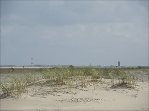 Sand dunes with grasses in the foreground and a lighthouse in the distance under a cloudy sky, sand