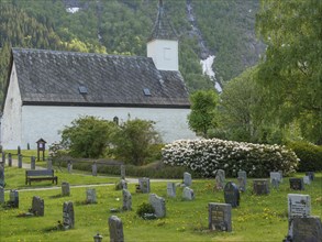 Cemetery with a church and gravestones surrounded by green trees and a mountain landscape,