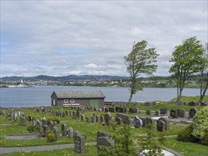 Cemetery with many gravestones, a small lake and a house under a partly cloudy sky, old stone