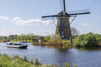 Windmill on a river with a boat and tree in the background on a sunny day, many historical
