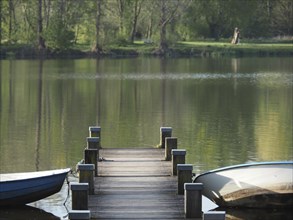 Wooden jetty leading into the water with two rowing boats on a quiet lake in a green environment,