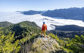 Mountaineer on the rocky summit of the Ettaler Manndl, view over mountain landscape and sea of