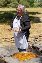 Cook with white apron collecting wood for the fire in the field to make a typical spanish paella