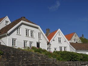 Houses with white wooden facades and red roofs standing against a stone wall under a clear blue