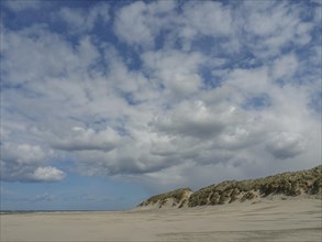 Spacious beach with cloudy sky, view of sand dunes along the coastline, beach and dunes with grass