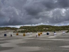 Cloudy sky on the beach with lonely beach chairs, dunes in the background, colourful beach chairs