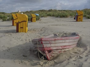 Abandoned boat in the sand, surrounded by beach chairs and dunes, cloudy sky in the background,