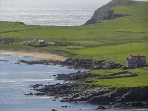 Coastal scene with green hills and a single house by the sea, green meadows by a deep blue sea and