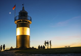 Black and white lighthouse, called 'Kleiner Preusse', stands illuminated at night shortly after