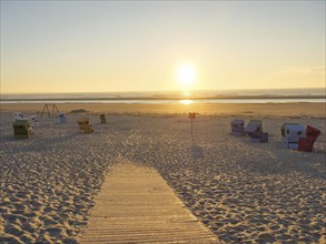 Sunset over the sea with beach chairs and wooden walkway on a sandy beach in a quiet atmosphere,