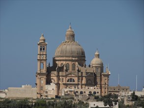 A large baroque basilica with a dome and detailed sandstone architecture set against a blue sky,