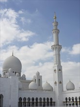 Magnificent mosque with several domes and a high minaret under a cloudy sky, large mosque with