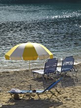 Yellow and white parasols and deckchairs on the beach with glittering sea in the background,