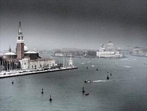A distant view of a church and boats on the water of Venice on a cloudy day, church towers and