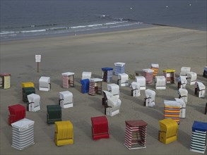 Several colourful beach chairs are spread out on the sandy beach under a cloudy sky, beach chairs