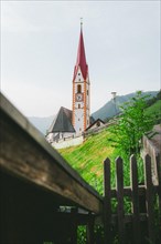 Church with a red pointed roof and a clock on a green hill. Nauders, Austria, Europe