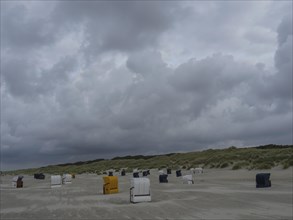 Beach chairs spread over the cloudy beach, with dunes in the background, colourful beach chairs on