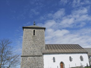 Historic church with stone tower and blue sky, some clouds in the background, old stone church and