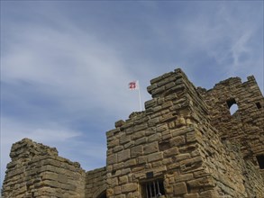 The top of a historic castle with stone towers and a waving flag under a cloudy sky, ruins and old
