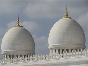 Close-up of two large white domes with golden tips under a partly cloudy sky, beautiful mosque with