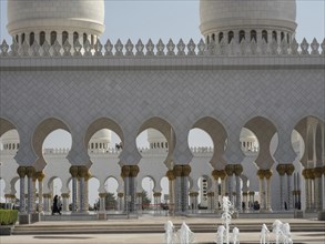 Mosque with arches and ornately decorated columns under a clear sky and visible fountains,