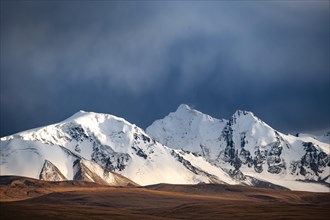 Glaciated and snow-covered mountains, dramatic landscape in the evening light with dark clouds,