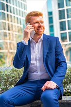Vertical photo of an elegant businessman talking to the mobile sitting outside the office in the