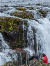 Two people sit near a picturesque waterfall and enjoy nature, Iceland, Europe
