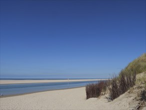 A lonely beach with dunes in the foreground, the sea with waves and the clear blue sky creates a
