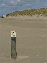 Close-up of a numbered post in a sandy coastal area under a cloudy sky, clouds on the beach with