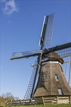 Windmill in front of a blue sky with scattered clouds on a sunny day, windmill with a fence in