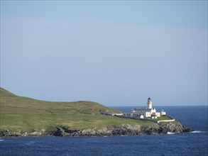 Lighthouse on the coast, surrounded by grassy hills and blue sea under a clear sky, white
