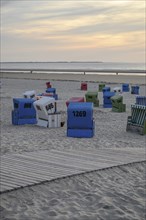 Beach chairs and a wooden path on a sandy beach at sunset, many colourful beach chairs on a warm