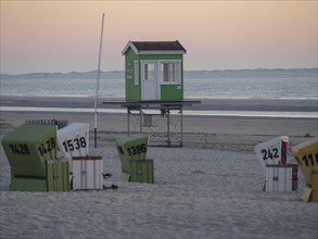 Green beach hut and colourful beach chairs in the sand by the sea at dusk, sunset on a quiet beach
