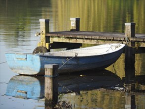 A blue boat is moored at the jetty and reflected in the still waters of the lake, rowing boats and