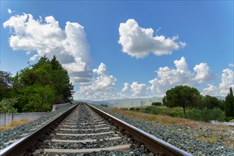 Train track going towards a mountain with a blue sky with clouds