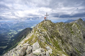 Mountaineer on the rocky pointed summit of the Raudenspitze or Monte Fleons with summit cross,