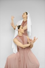 Two female dancers perform hand movements on grey background