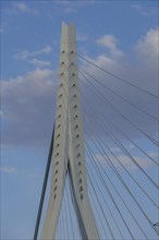 Modern cable bridge segment, against the blue sky with scattered clouds, skyline of a modern city