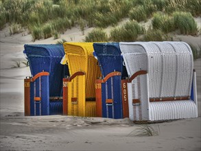 Close-up of colourful beach chairs made of rattan in blue, yellow and white in a dune landscape,